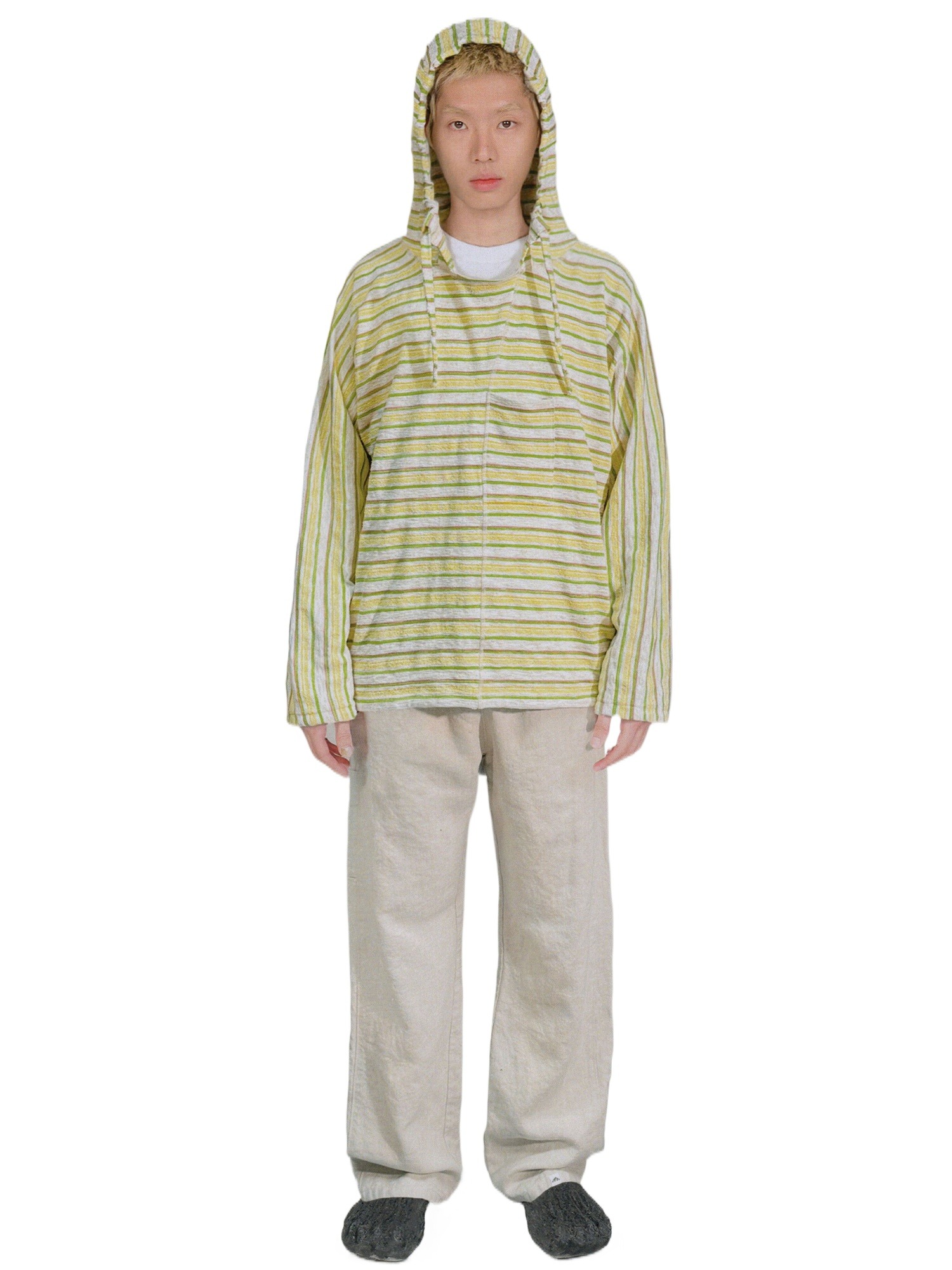 一个人穿着 EastLyst Baja 款式的针织套头衫,黄绿条纹相间,带帽,搭配多种米色裤子和徒步鞋,面向前方。背景为纯白色。