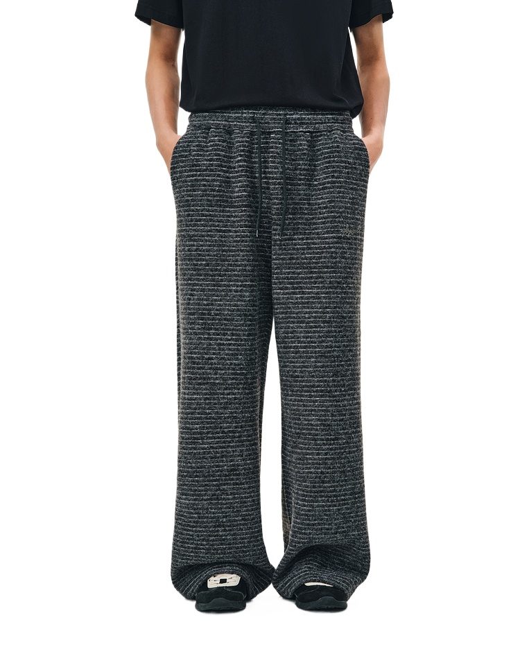 A person wears EastLyst Retro Athletic Pants—loose, dark gray vertical stripes, drawstring waist, 400GSM fabric—with hands-in-pockets styling; paired with a black shirt and slippers. Face is not visible.