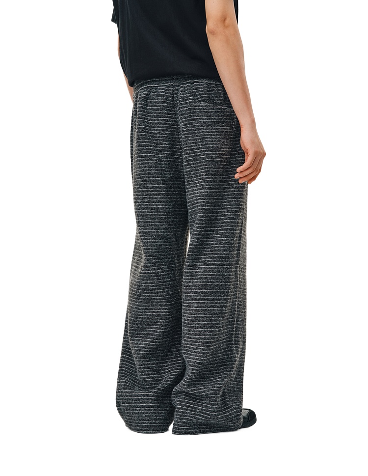A person models EastLyst's Retro Athletic Pants—loose-fitting with dark gray vertical stripes—paired with a black top, standing in profile and back view against a white background.