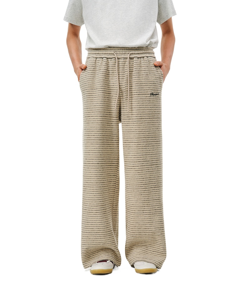 A person wearing EastLyst Retro Athletic Pants—loose beige 400GSM trousers with subtle horizontal stripes—is shown from the waist down, hands in pockets.