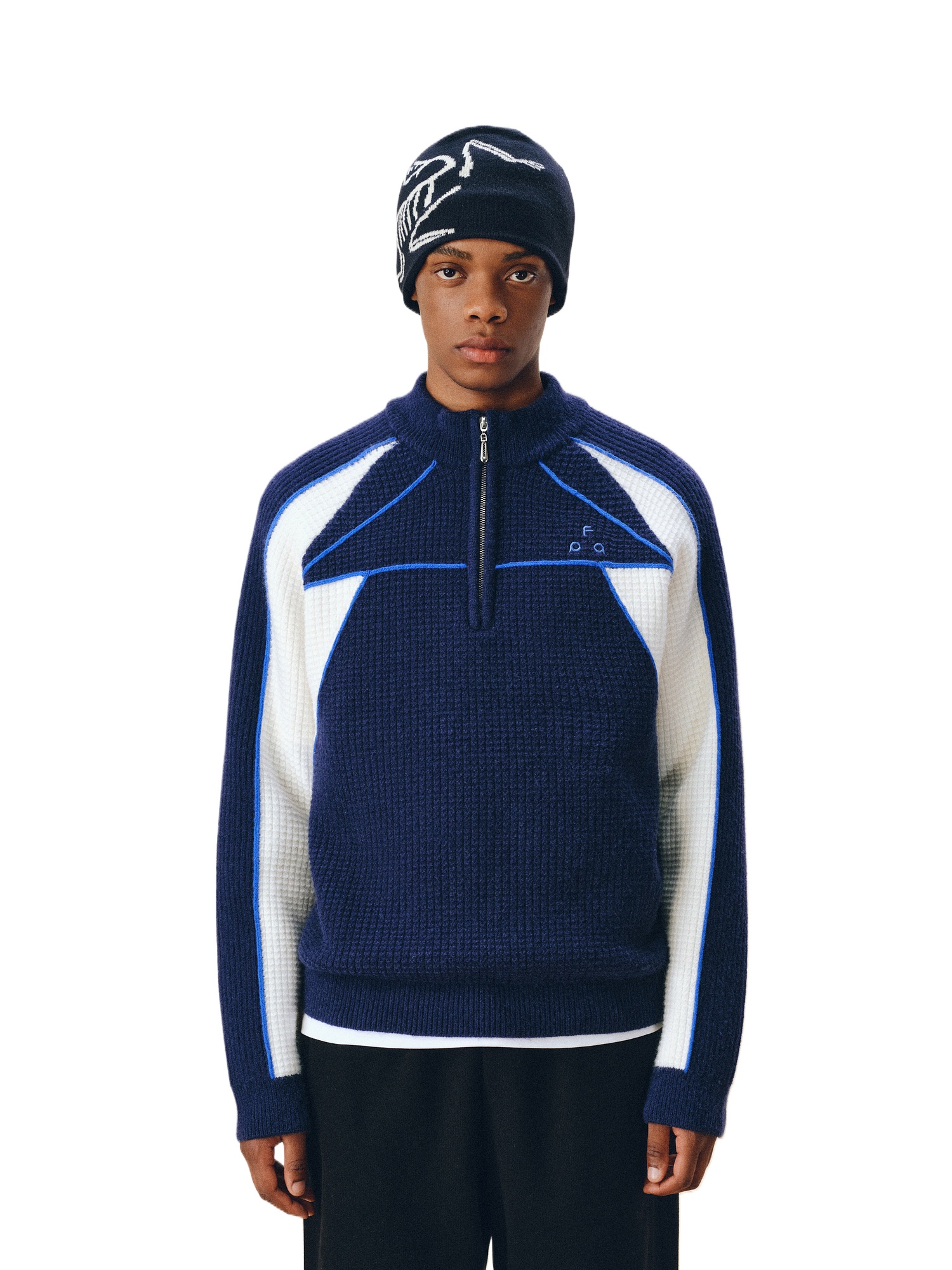 Wearing the EastLyst Color Block Half Zip Sweater, styled with black pants and a black knit hat, a person stands against a white background, highlighting the sweater’s premium warmth and geometric design.