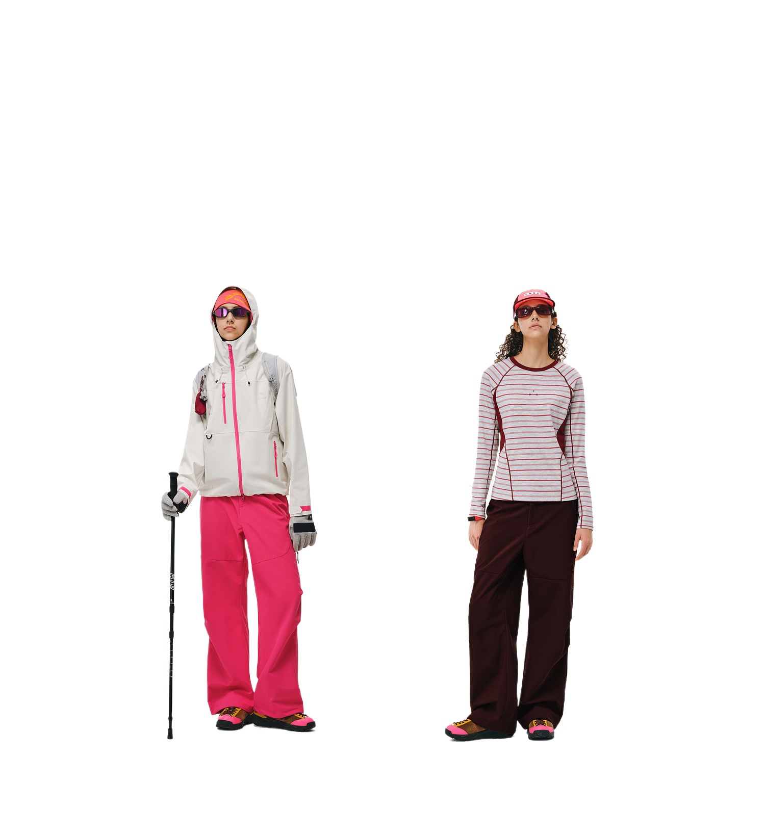 Two people stand side by side in outdoor gear; the left wears EastLyst Softshell Trousers for Hiking, a hooded jacket, and holds a trekking pole. The right wears a striped long-sleeve shirt and dark pants. Both wear sunglasses and hats.