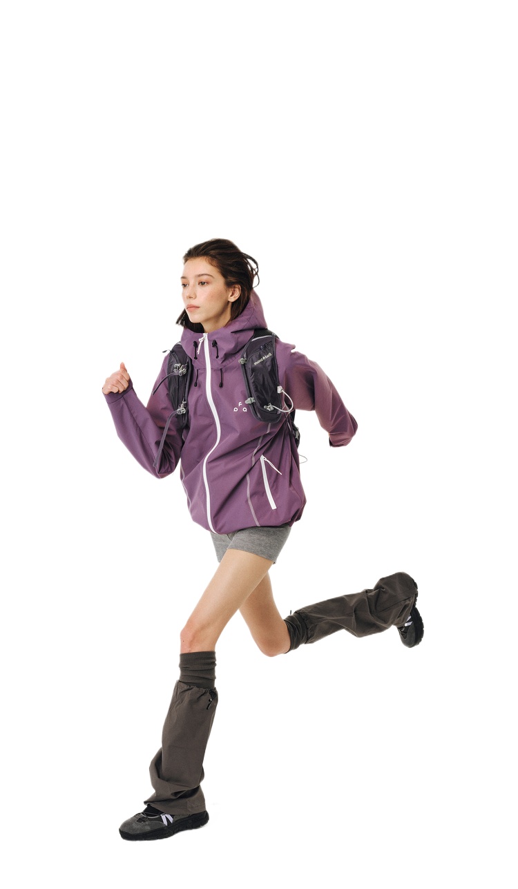 A woman in an EastLyst protective outdoor jacket runs, paired with gray shorts, brown gaiters, a black backpack, and black shoes, isolated on a white background.